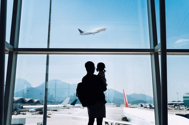 快乐的年轻亚洲父亲带着可爱的小女儿在机场等候起飞时透过窗户看飞机的剪影