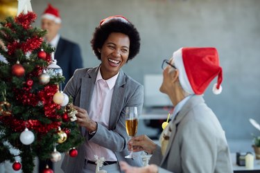 性格开朗的黑人女商人和她的同事在办公室装饰圣诞树时玩得很开心。